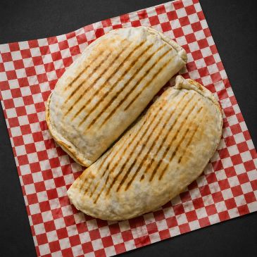 Two grilled wraps on a red and white checkered paper.