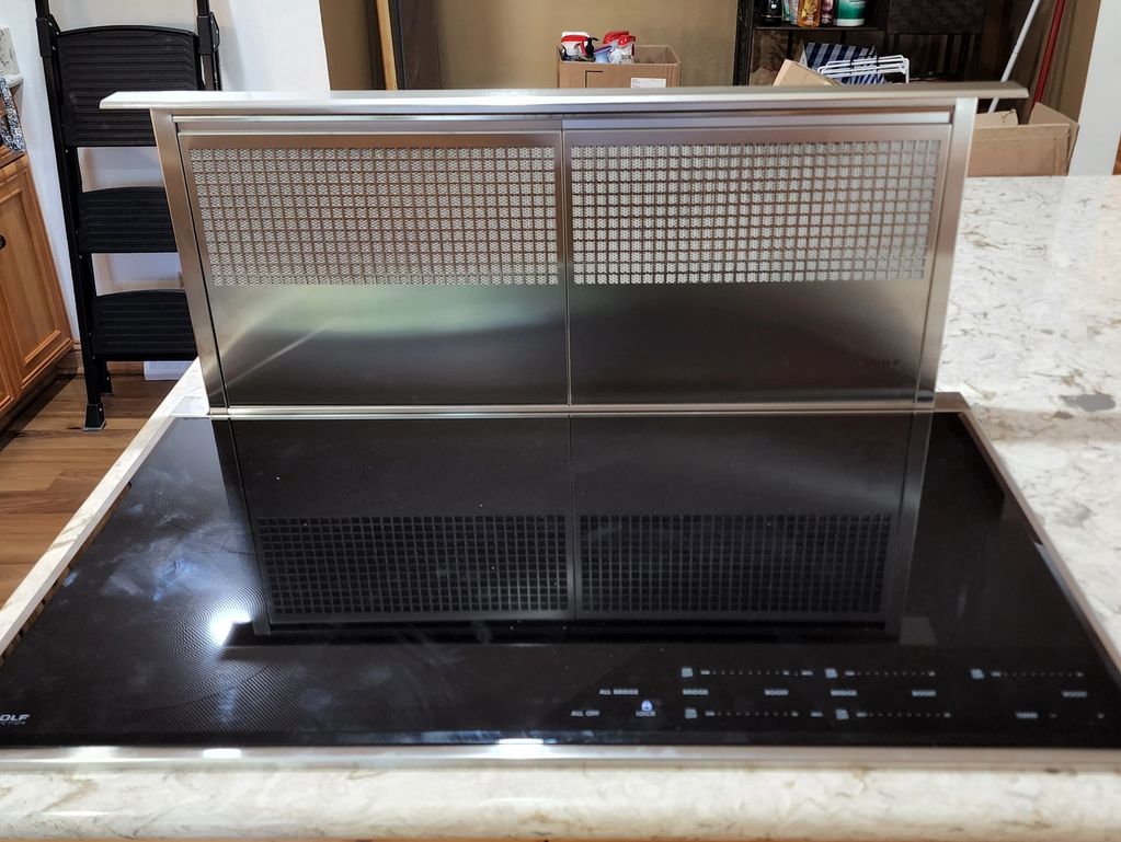 Modern kitchen cooktop with a built-in retractable vent on a marble countertop.