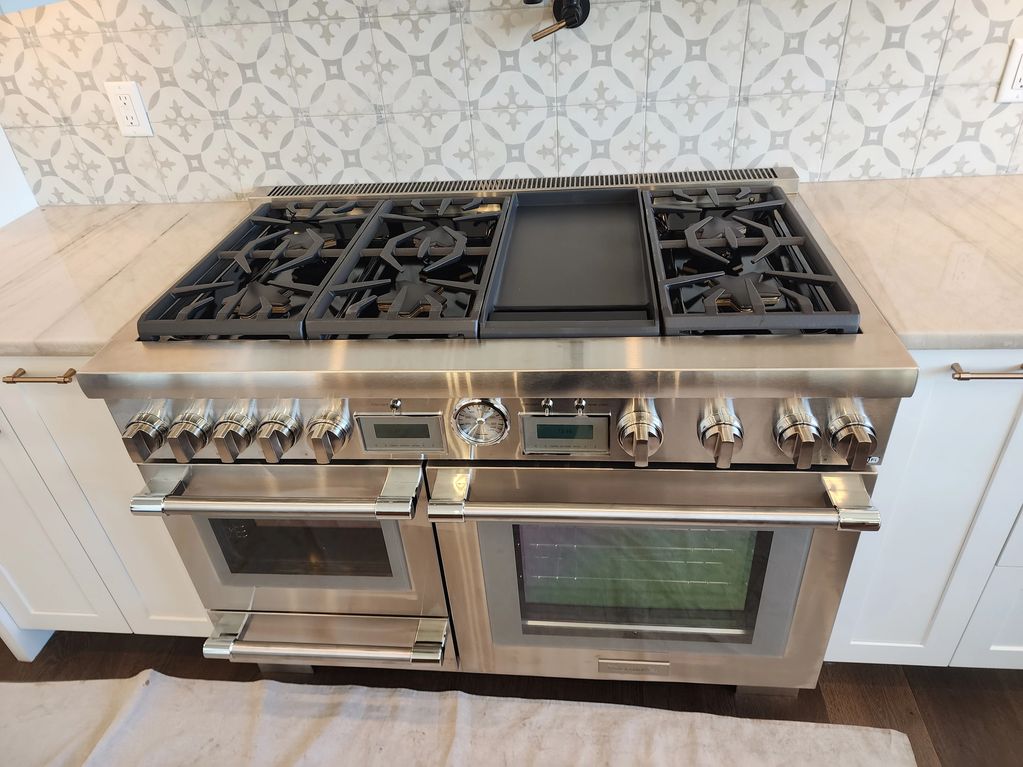 Luxury stainless steel stove with multiple burners and ovens in a modern kitchen.