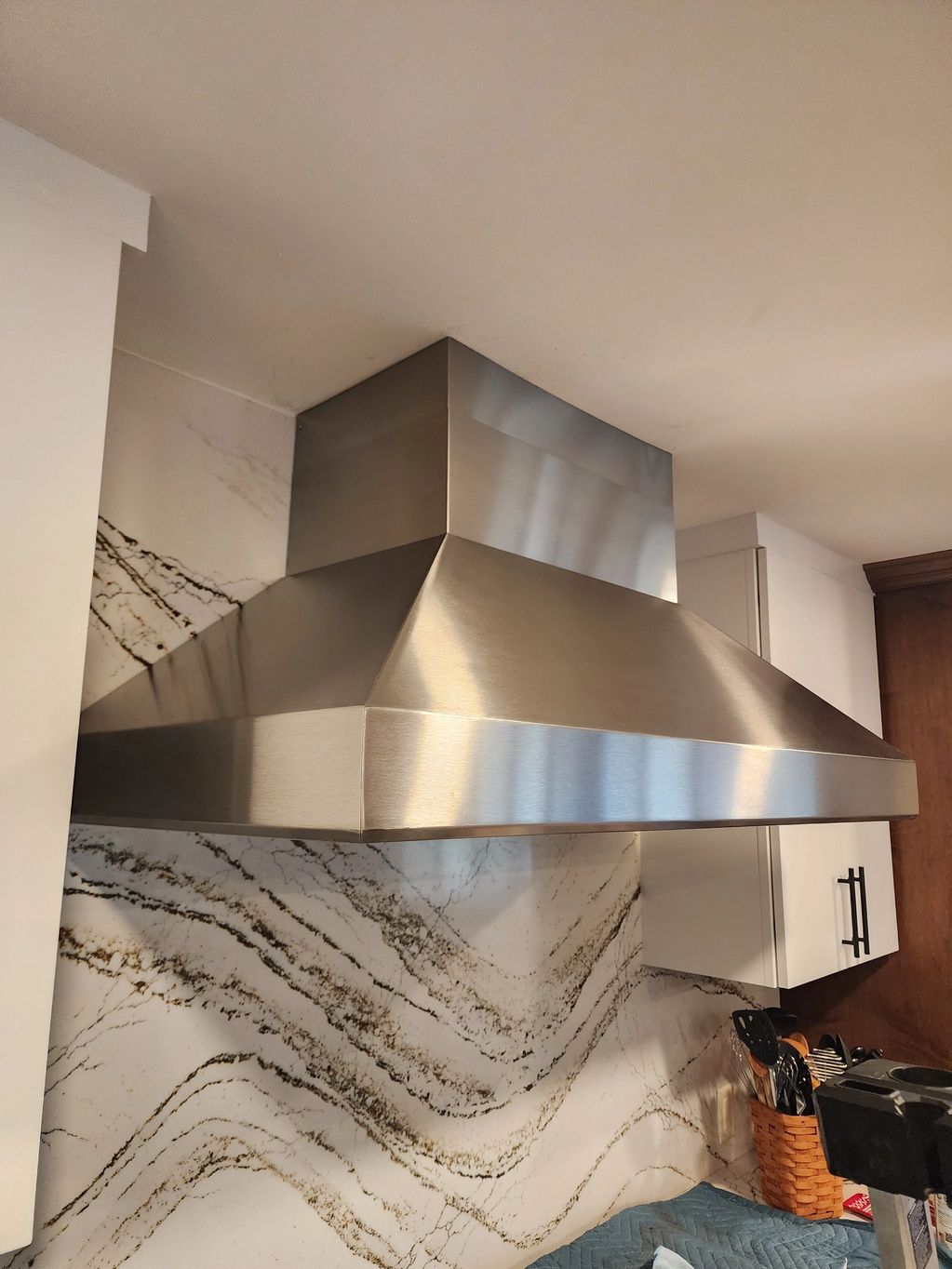 Modern stainless steel kitchen range hood with marble backsplash.