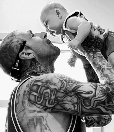 Tattooed man lovingly holding a baby, sharing a joyful moment.