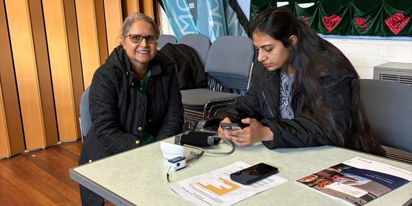 Two women seated at a table, one smiling and the other focused on her phone.