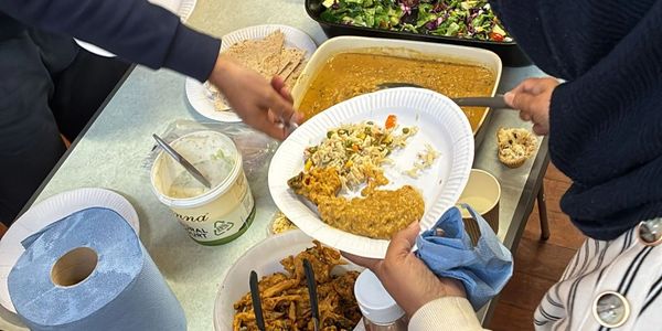 People serving and holding plates of food at a buffet-style meal.