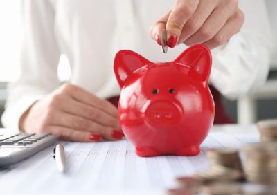 Woman putting coin into red piggy bank to increase her savings