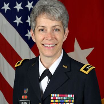 Female military officer in uniform with medals and flags in the background.