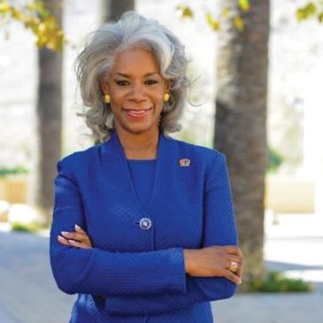 Confident woman in a blue suit smiling with arms crossed outdoors.