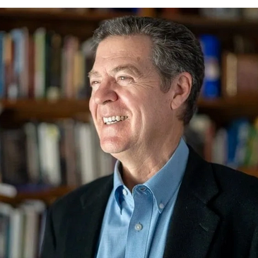 Smiling man in a blue shirt and black blazer, looking sideways.