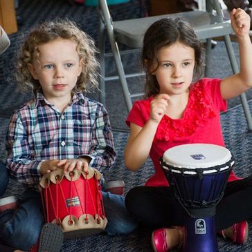 Three children playing different drums while sitting on the floor.