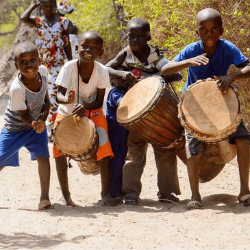 Four boys playing traditional drums outdoors on a sunny day.