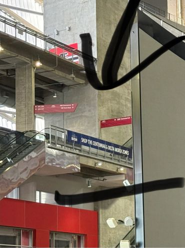 Concrete interior with escalators and signs for Centennial and Delta merch zones.
