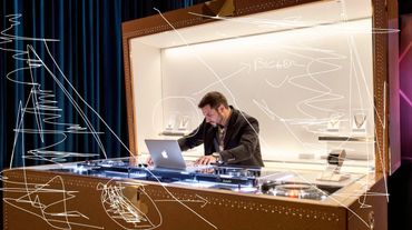 A DJ in a display case with luxury jewelry and Apple laptop.