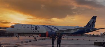 Delta Airlines plane celebrating 100 years, parked at sunset with two workers nearby.