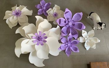 Large white and purple paper flowers arranged on a floor with a small dog nearby.