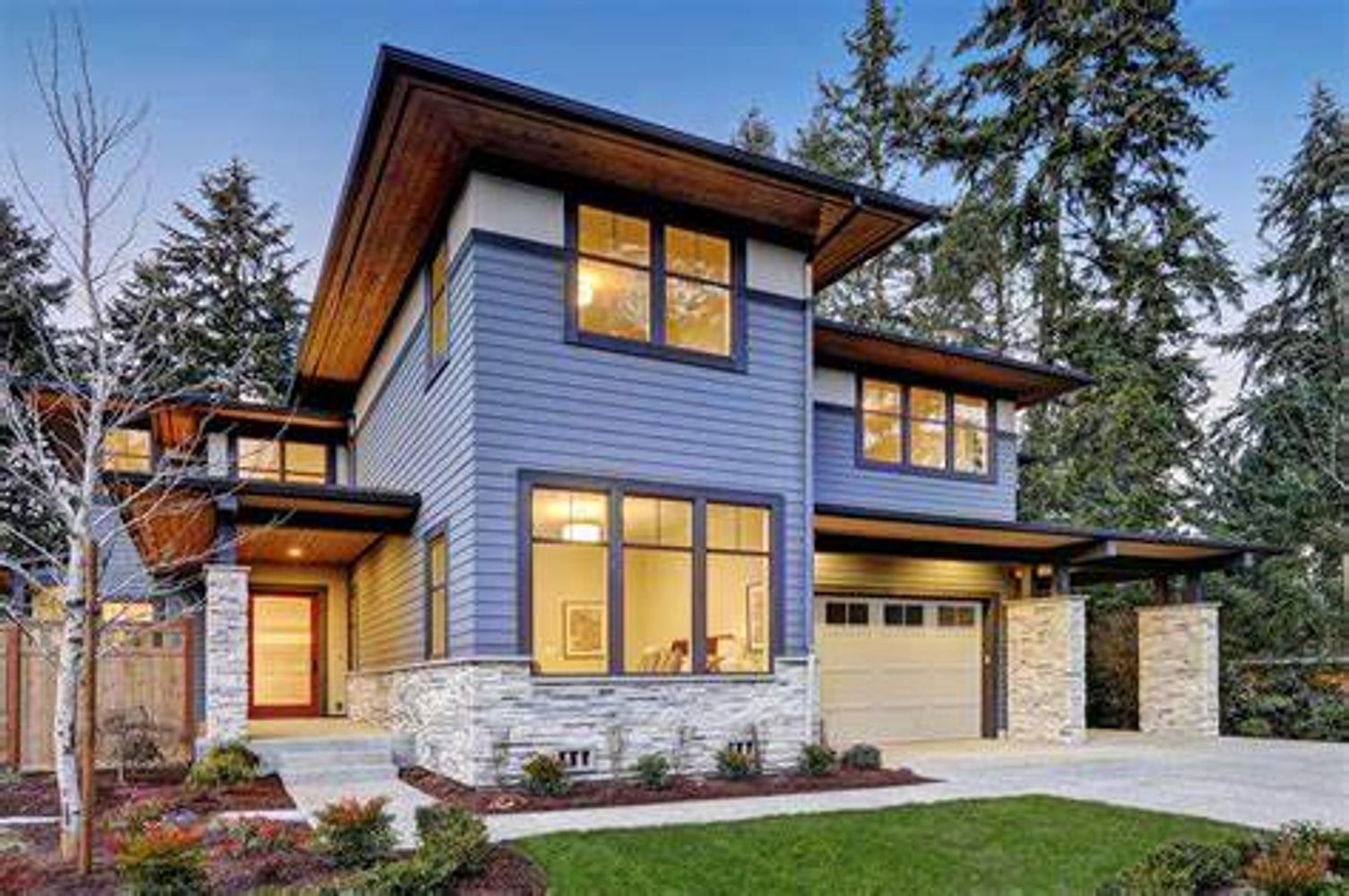 Modern two-story house with blue siding and warm interior lights.