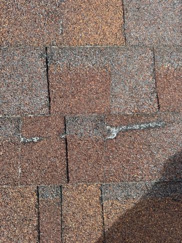 Close-up of weathered asphalt roof shingles with a visible crack.