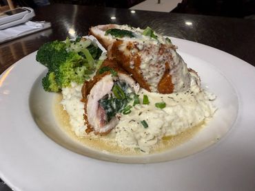 Stuffed chicken breast with creamy sauce, mashed potatoes, and broccoli on a white plate.