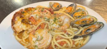 Seafood pasta with shrimp, mussels, and herbs on a white plate.