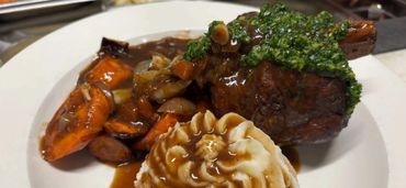 A plated meal with mashed potatoes, roasted carrots, and steak topped with green herb sauce.