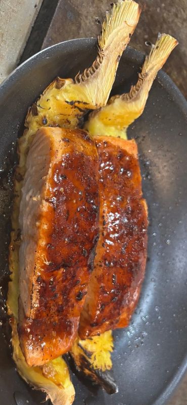 Two perfectly seared salmon fillets on grilled pineapple slices in a pan.