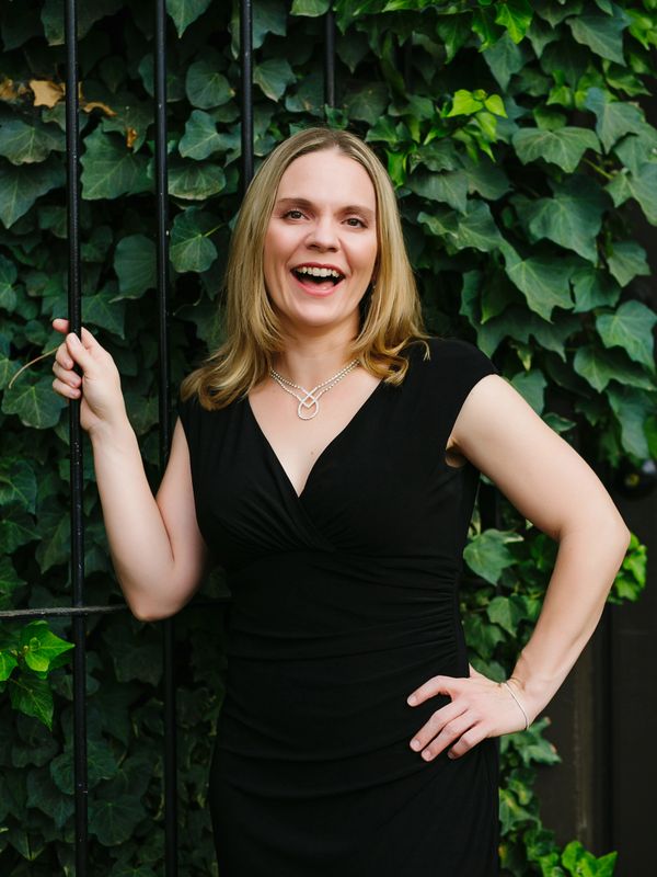 Molly Holleran, soprano and voice teacher, laughing in front of an ivy-covered fence