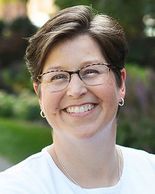 Smiling woman with short brown hair and glasses outdoors.