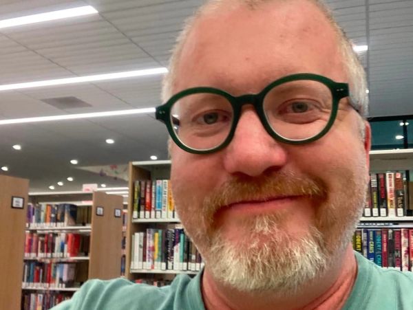 Man with glasses smiling in a library.