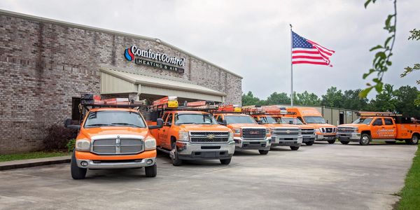 Comfort Control Heating, Air, and refrigeration orange trucks outside in front of the building.