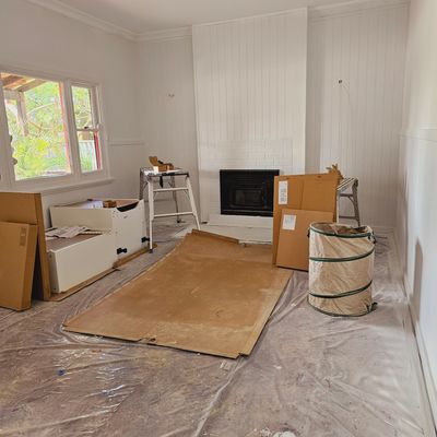 Room under renovation with covered floor and packed furniture.