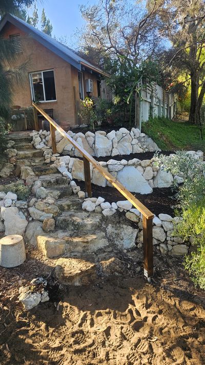 Stone garden bed with wooden railing near a house under clear sky.