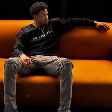 Man in casual wear sitting on an orange couch, looking to the side.