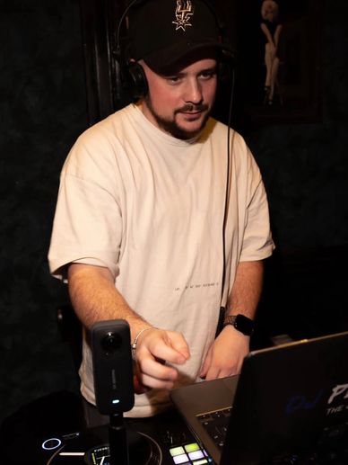 A DJ wearing headphones and a cap, mixing music on a laptop and turntable.