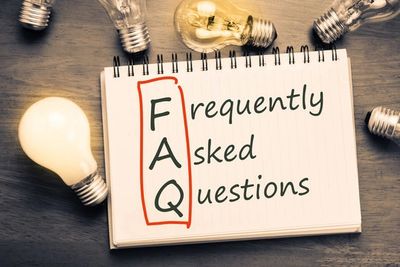 Notebook with FAQ acronym surrounded by light bulbs on wooden surface.