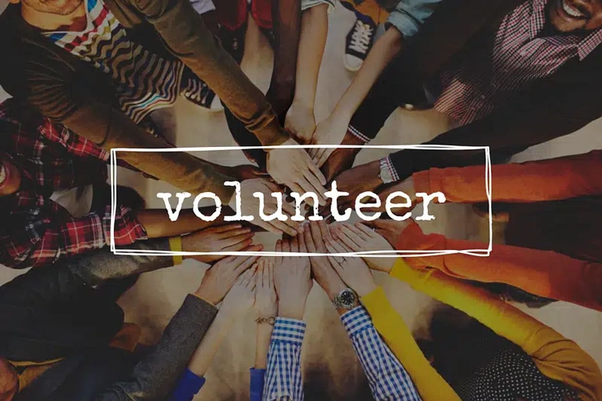 Diverse group of people joining hands in unity with 'volunteer' text overlay.
