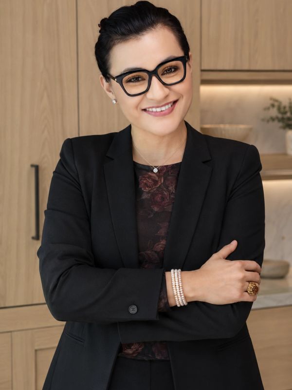 Confident woman in black suit smiling with arms crossed.