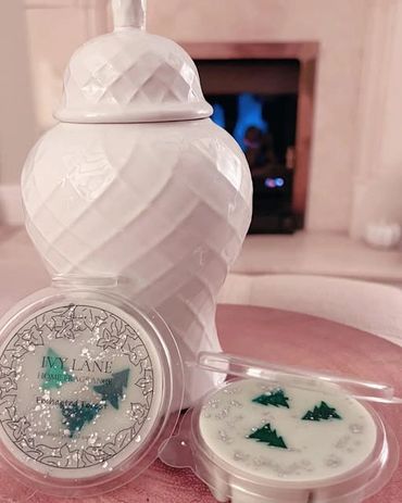 Decorative wax melts with Christmas tree shapes and a white ceramic jar on a pink surface.