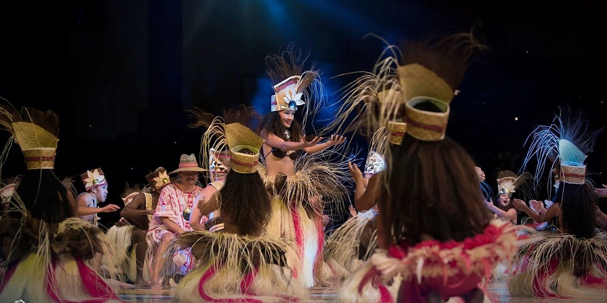 Traditional Polynesian dance performance with dancers in grass skirts and elaborate headdresses.