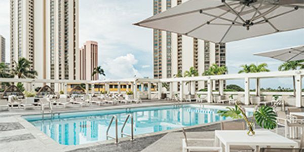 Modern outdoor pool area with umbrellas and high-rise buildings in the background.
