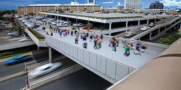 Pedestrian bridge over a busy road with people walking and cars passing underneath.