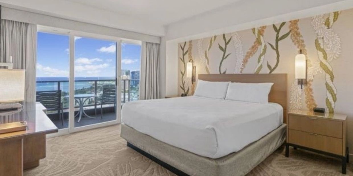 Modern hotel room with king-size bed and balcony ocean view.