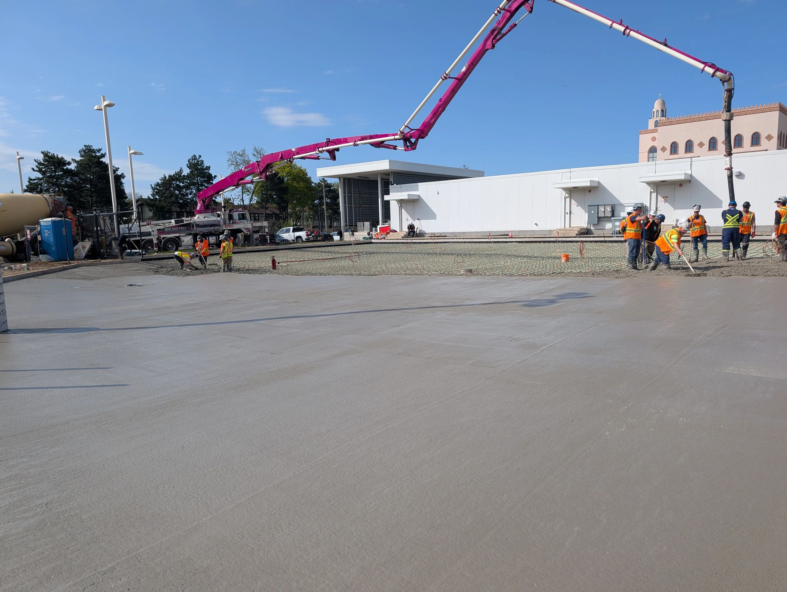 Construction workers pouring and smoothing concrete at a building site on a clear day.