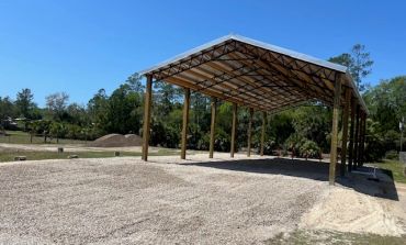 Open metal pavilion with gravel floor under a clear blue sky.