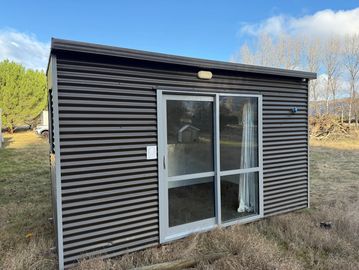 Small modern shed with sliding glass door in a grassy area.