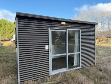 Small modern shed with sliding glass door in a grassy area.