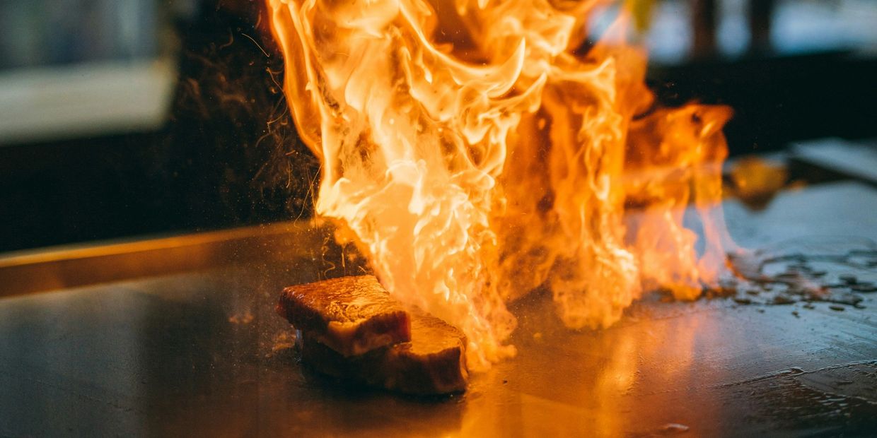 Flames engulfing a steak on a grill during cooking.