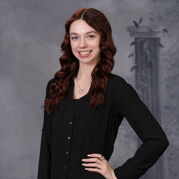 Young woman with curly auburn hair smiling, wearing a black blouse.