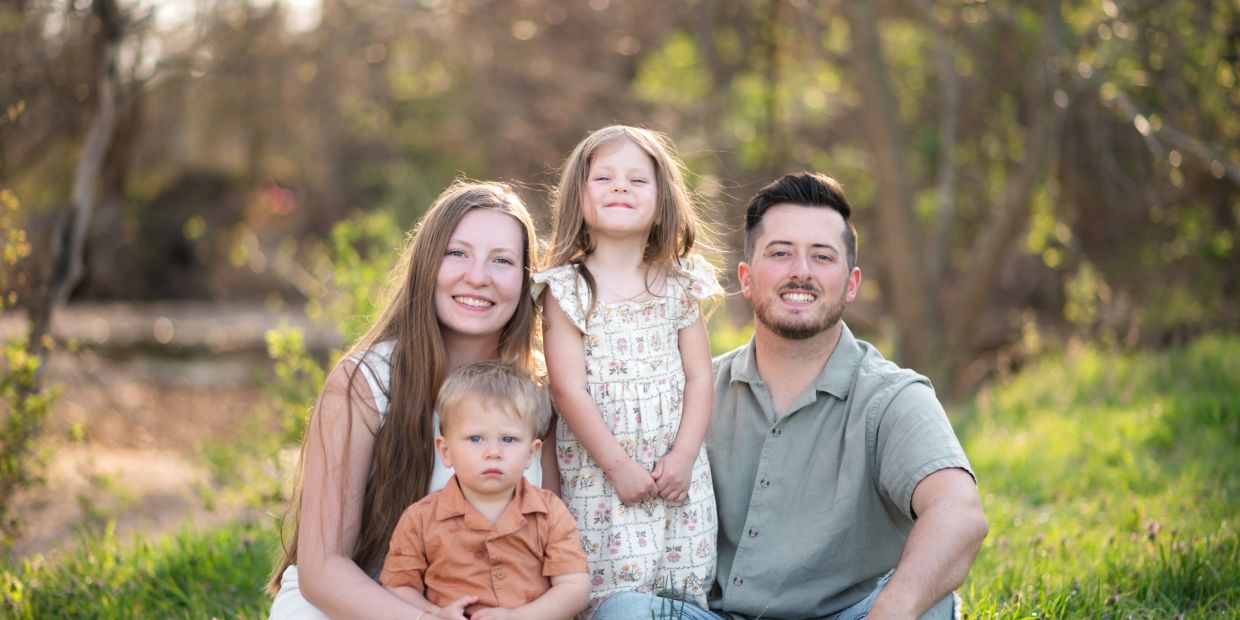 A happy family of four posing outdoors in nature.
