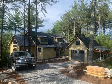 Yellow house with a black pickup truck parked on a gravel driveway surrounded by trees.