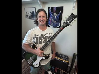 Man smiling with electric guitar and The Beatles T-shirt.