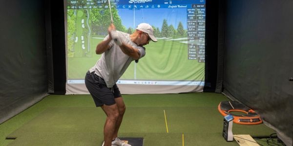 Man practicing golf swing indoors with a golf simulator.