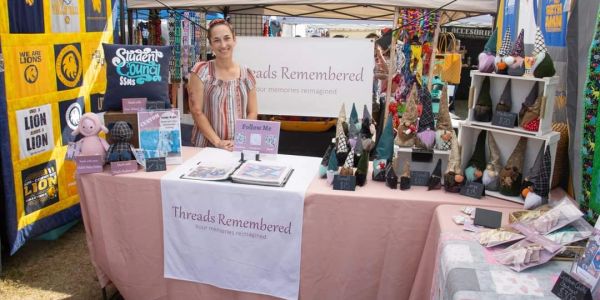 Woman showcasing handmade crafts under a tent at a fair.